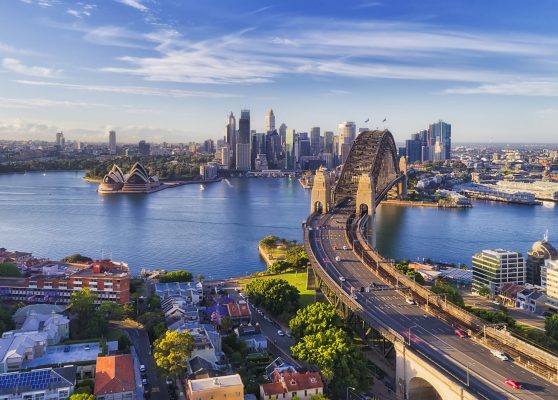 D Sydney Kirribilli HWY Br CBD Cahill express way to the Sydney Harbour bridge across Sydney harbour towards city CBD landmarks in aerial eleveated wide view under blue morning sky.